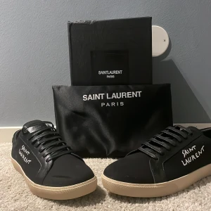  Saint Laurent court  - Snygga svarta sneakers från Saint Laurent med vit sula och märkets logotyp i vitt på sidan. Skorna har snörning och är tillverkade i skinn, vilket ger en lyxig känsla. Perfekta för en stilren look. Kvitto finns ! Om ni är intresserade 