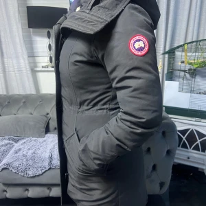Svart parkajacka från Canada Goose - Säljer en svart parkajacka från Canada Goose med pälsdetalj på huvan. Jackan har en figurnära passform och långa ärmar. Perfekt för kalla dagar med sin varma och skyddande design. 🖤