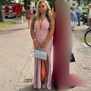 Rosa glittrig långklänning - Säljer en fantastisk rosa glittrig långklänning med djup v-ringning och slits. Den har en mycket fin snörning på baksidan. Använd endast en gång då detta var min balklänning på studenten!🤗💗