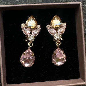 Glittriga örhängen med rosa stenar (CLIPS ÖRHÄNGEN) - Eleganta örhängen med stora droppformade rosa stenar och mindre klara stenar i en guldinfattning. Perfekta för att ge en glamorös touch till din look. Endast testade. Fick i present (box medföljer)