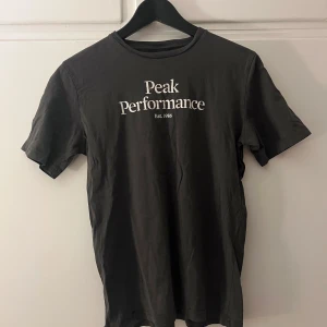 Grå/grön t-shirt från Peak Performance - Säljer en grå/grön t-shirt från Peak Performance med tryck på framsidan. T-shirten är kortärmad och tillverkad i bomull. Perfekt för en avslappnad stil. Tyvärr defekt med två hål längst ned i sidan…