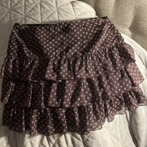 Brun volangkjol från Zara - Säljer en söt brun volangkjol från Zara med små vita blommor. Kjolen har flera lager volanger, passar perfekt till sommaren!!  Super fint skick. Stl Xs 