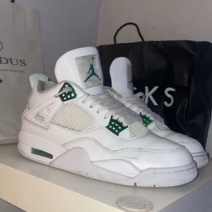 Jordan 4 metallic green  - Snygga vita Nike Air Jordans med gröna detaljer. Skorna har en klassisk design med snörning och det ikoniska Jumpman-logotypen i grönt. Perfekta för dig som vill ha en stilren look med en touch av färg.