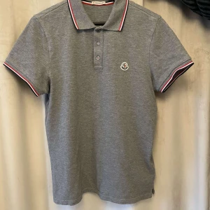 Moncler pikétröja - Grå piké från Moncler i jätte fint skick. Köpt från NK för något år sedan och knappt använd sedan dess. Röda vita och blå detaljer.