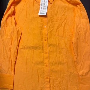 Orange skjorta - Snygg orange skjorta med klassisk krage och knappar framtill. Perfekt för att liva upp garderoben med en färgklick. Skjortan har en bröstficka och långa ärmar.