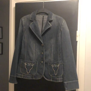 Jeanskavaj med broderade fickor - Snygg jeansjacka med broderade detaljer på fickorna. Jackan har en klassisk krage och knäpps med tre knappar framtill. Perfekt för en avslappnad stil med en touch av unik design.