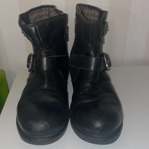 Svarta boots från Replay - Snygga svarta boots från Replay i skinn med dekorativa spännen och dragkedja på sidan. Perfekta för en cool och avslappnad stil. Insidan har ett mönstrat foder som ger en extra touch.