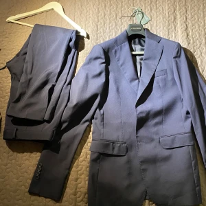 Mörkblå kostym från Cavaliere (pris vid förfrågan)  - Pris vid förfrågan. Snygg mörkblå kostym från Cavaliere i storlek 48. Kavajen har klassisk design med knappar och byxorna matchar perfekt. Perfekt för formella tillfällen. Ärmarna är förlängade på kostymen, vilket enkelt kan förkortas igen. Använts en gång då jag växte snabbt ut ur kostymen tyvärr. Väldigt fin kostym vilket jag skulle vilja ha kvar men den blev för liten. Tveka inte att ställa fårgor. Jag har fler bilder. 
