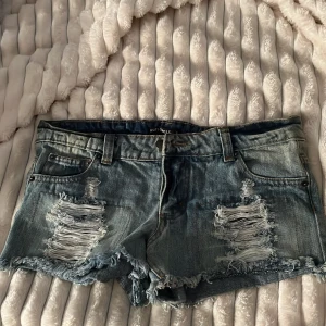 Blå lågmidjade jeansshorts från Rut&Circle - Snygga blå jeansshorts från Rut&Circle med slitna detaljer och fransiga kanter. Shortsen har flera knappar och är i storlek 36. Shortsen är har använts en gång. Vill ni ha bilder på så får ni fråga💗