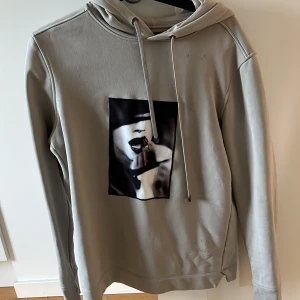Grå Limitato hoddie - Snygg grå hoodie med ett unikt tryck på framsidan från Ellen von Unwerth. Tröjan har en klassisk huva med dragsko och långa ärmar. Perfekt för en stilren och bekväm look.