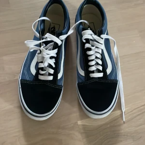 Blå och svarta sneakers från Vans storlek: 40 - Snygga blå och svarta sneakers från Vans med vit sula och klassisk vit sidostrimma. Skorna har snörning och är perfekta för en avslappnad stil.           är oandvända.