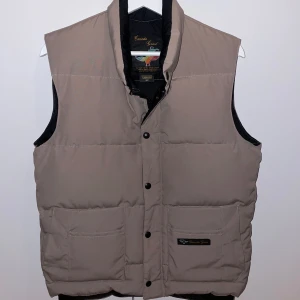 Canada Goose dunväst - Säljer en schysst beige dunväst från Canada Goose. Använd någon enstaka gång och sedan hängt i garderoben bara så den är i nyskick. Storlek S och true to size. Nypris runt 6000kr. Skriv om det finns frågor, pris kan diskuteras.