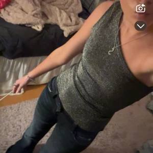 Glittrig oneshoulder topp - Snygg glittrig oneshoulder topp i silver. Perfekt för en utekväll eller fest. Toppen har en tight passform som framhäver figuren.