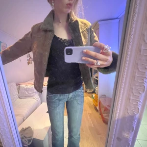 Beige mockajacka med pälsdetaljer - Snygg beige mockajacka med pälsdetaljer på kragen och ärmsluten. Jackan har en stilren design med knappar framtill och en croppad passform. Perfekt för höst och vår! (Obs finns pytteliten fläck vid vänster arm)