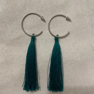 Silvriga örhängen med gröna fransar - Snygga silvriga örhängen med långa gröna fransar som ger en bohemisk touch. Perfekta för att lägga till en färgklick till din outfit. Örhängena har en enkel ringdesign som gör dem lätta att bära. Längd 11cm