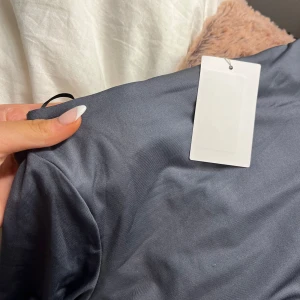 Grå/blå glansig långärmad bodysuit - Säljer en stilren grå långärmad bodysuit med en rakhals. Perfekt för lager-på-lager eller att bära som den är. Materialet är mjukt och stretchigt för en bekväm passform, den här helt ny med prislapp kvar💞💞