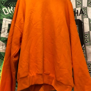 Orange sweatshirt med Los Angeles-tryck - Cool orange sweatshirt med svart Los Angeles-tryck över bröstet. Tröjan har långa ärmar och en avslappnad passform, perfekt för en casual look.