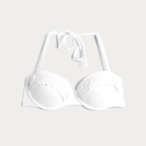 Vit bikiniöverdel med spetsdetaljer - Snygg vit bikiniöverdel med bygel, spetsdetaljer och broderade blommor. Den har knytband i nacken  som enkelt kan tas av och bäras som en bandeau bikini. Perfekt för en stilren look på stranden. Köpt på cubus för 249kr. Mycket bra skick endast använd en gång. Hör av dig vid frågor💞