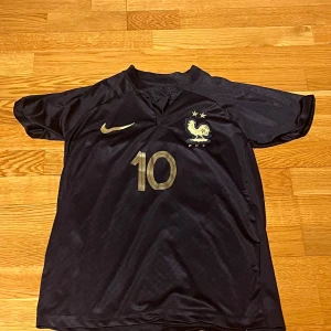 Svart fotbollströja från Nike - Snygg svart fotbollströja från Nike med guldiga detaljer. Tröjan har korta ärmar och nummer 10 på både fram- och baksidan. Perfekt för fotbollsfans!