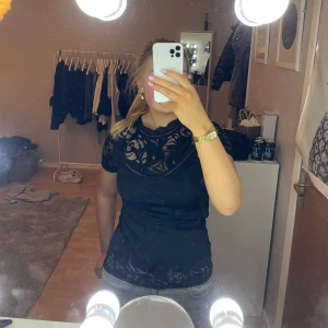 Svart spetsblus från Vila - Svart spetsblus från Vila med korta ärmar och rund hals. Blusen har ett spetsmönster och en dragkedja i ryggen. Perfekt till exempelvis fest💕