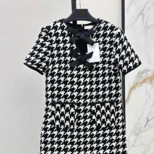 Svartvit rutig klänning med rosett - Snygg svartvit rutig klänning med korta ärmar och dekorativ rosett framtill. Klänningen har två fickor och en klassisk siluett som passar perfekt för en chic look.