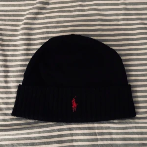 Svart mössa från Ralph Lauren - svart mössa från Ralph Lauren (äkta) med röd broderad logga framtill. (ANVÄND 1 GÅNG). Priset går att diskutera.