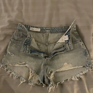 Ljusa jeansshorts från Zara - Snygga ljusa jeansshorts från Zara med slitna detaljer och fransiga kanter. Perfekta för en avslappnad stil. De har en klassisk femficksdesign och knappgylf.