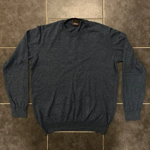 Mörkblå tröja från Oscar Jacobson - Säljer en stilren mörkblå tröja från Oscar Jacobson. Tröjan har en rund hals och långa ärmar, perfekt för en klassisk look. Tillverkad i Italien med högkvalitativt material.