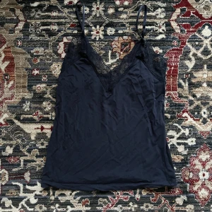 Mörkblått linne med spetsdetaljer! - Snyggt mörkblått linne med smala axelband och v-ringning dekorerad med spets. Inga lappar men i storlek xs, och i använt med bra skick! Så otroligt skönt material 🤍Perfekt för en stilren look.