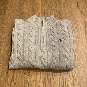 Grå stickad tröja från Polo Ralph Lauren - Tja! Säljer en stilren grå stickad tröja från Polo Ralph Lauren med kabelstickat mönster och dragkedja vid halsen. Stl M men sitter som S. Skick 10/10!! Skriv till mig vid fler frågor! 😁
