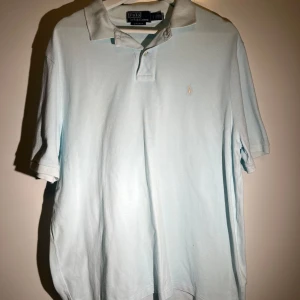 Ljusblå pikétröja från Ralph Lauren - Säljer en stilren ljusblå pikétröja från Ralph Lauren. Tröjan har en klassisk krage och korta ärmar, perfekt för en avslappnad men ändå snygg look. Den ikoniska loggan är broderad på bröstet. Passar utmärkt till både jeans och chinos. Köpte på NK för 1500, knappt använt då den va lite stor. 