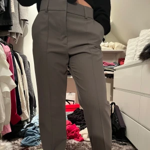 Grå kostymbyxor - Snygga grå kostymbyxor med hög midja och raka ben. Perfekta för en stilren look. Byxorna har en klassisk design med knappar och dragkedja framtill.