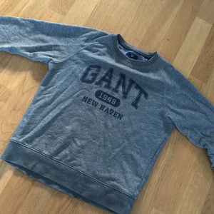 Grå sweatshirt från GANT - Säljer en grå sweatshirt från GANT med tryck '1949 New Haven' på framsidan. Tröjan har långa ärmar och en rund halsringning. Perfekt för en avslappnad stil.