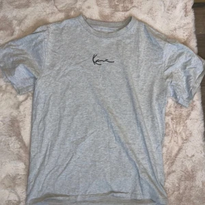 Grå t-shirt från Karl Kani - Säljer en stilren grå t-shirt från Karl Kani i storlek L. T-shirten har en enkel design med korta ärmar och ett diskret tryck på bröstet. Perfekt för en avslappnad look.