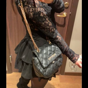 Svart quiltad valentino axelväska med kedja - Snygg svart quiltad axelväska med guldfärgad kedja. Perfekt för en kväll ute eller en dag på stan. Väskan har en elegant design och är lätt att matcha med olika outfits.