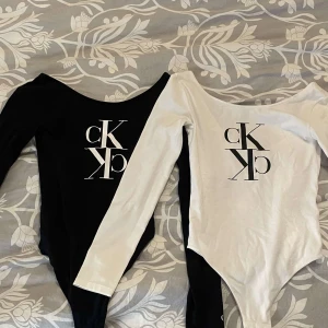 Långärmad body från Calvin Klein - Två stilrena långärmade toppar från Calvin Klein i svart och vit. Båda topparna har en stor CK-logga på framsidan och en elegant, åtsittande passform. Aldrig använt💕150 styck💕 ordinarie pris runt 800kr styck💕