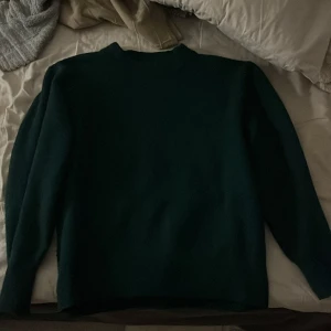 Mörkgrön tröja - Säljer en stilren stickad mörkgrön tröja med långa ärmar. Perfekt för kyligare dagar och enkel att matcha med olika outfits. Varm och mjuk och den sticks inte.
