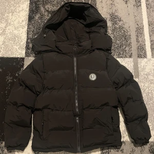 Svart Pufferjacka Från Trapstar - Säljer en Svart Pufferjacka från Trapstar med huva och dragkedja. Jackan har ett broderat märke på bröstet och text på ryggen. Perfekt för kalla vinterdagar. Jag är 186cm och 62-67kg och bär M storlek och passar perfekt. Jackan är rätt tung och känns som en ordentlig jacka. Jag har använt jackan i bara 3 månader tagen finns inte kvar. .Priset kan diskuteras🙌