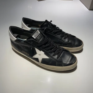 Golden Goose skor - Säljer mina svarta Golden Goose skor med vita detaljer. Skorna har en sliten design från fabrik men är använda. Låda, skopåsar och äkthetsintyg fås självklart med!
