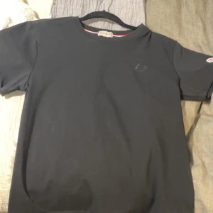 Svart t-shirt från Moncler - Säljer en stilren svart t-shirt från Moncler med deras ikoniska logga på ärmen. Perfekt för en avslappnad och trendig look. T-shirten är kortärmad och gjord i ett mjukt material. Storlek. M men kan också passa L beroende på 