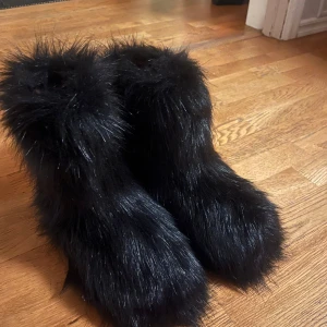 Svarta pälsiga boots - Säljer ett par unika svarta boots med pälsigt yttre. Perfekta för att hålla fötterna varma och stiliga under kalla dagar. De har en fluffig och iögonfallande design som verkligen sticker ut.