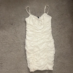 Vit spetsklänning med knytband - Säljer en söt vit spetsklänning från hm med smala axelband och knytband framtill. Klänningen har en åtsittande passform och är perfekt för sommarens fester. Den har ett vackert spetsmönster som ger en romantisk känsla.