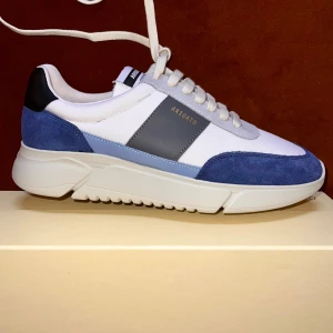 Sneakers från Axel Arigato - Snygga sneakers från Axel Arigato i vitt, blått och grått. Skorna har en modern design med snörning och en bekväm sula. Perfekta för en stilren look!                         Nypris 2600kr / 260 euro 