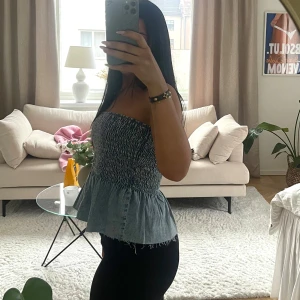 Blå axelbandslös topp - Snygg blå axelbandslös topp med smockdetaljer och volangkant. Perfekt för sommardagar och kan enkelt matchas med olika outfits. Den har en luftig passform och är tillverkad i ett lätt material.