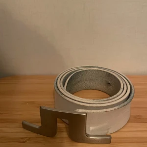 Vitt bälte från J Lindeberg med silverfärgat spänne - Snyggt vitt bälte från J Lindeberg med ett unikt silverfärgat spänne. Perfekt för att ge en stilren touch till din outfit. Bältet har en modern design och är tillverkat i ett slitstarkt material.