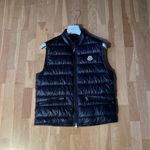 Moncler Gui Väst - Snygg mörk blå dunväst från Moncler modellen heter gui, storlek 3. Perfekt för lager-på-lager under kyliga dagar och för varmare vår och sommar dagar