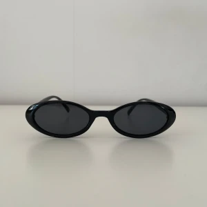Vintage solglasögon - oanvända svarta - Snygga svarta solglasögon med oval form. Perfekta för en stilren look. De har en glansig finish och smala skalmar som ger en modern touch.