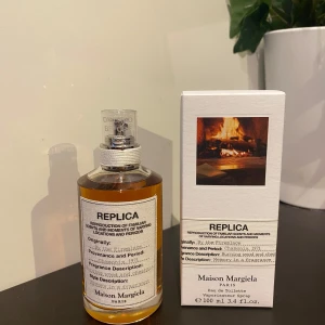Maison Margiela: By the fireplace 100ml - Maison Margiela: By the fireplace EDT, sprayats två gånger. Fick den i julklapp och säljer den då jag redan har en liknande parfym. Bifogade bilder visar vart den köptes från.  ”Doften har ett varmt hjärta av kastanj och träiga ackord blandat med söta noter av vanilj och röda bär. Den mjukas upp av den blommiga kombinationen av apelsinblommor och neroliessens.”