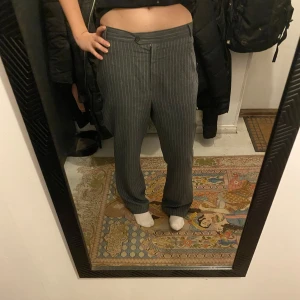 Grå randiga kostymbyxor - Snygga grå kostymbyxor med diskreta ränder. Byxorna har en klassisk passform med knapp och dragkedja framtill. Perfekta för en stilren look. Står att de är i storleken L men är nog snarare M. 