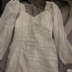 Vit klänning från NLY Trend - Vit klänning från NLY Trend med långa ärmar och v-ringad design. Jättefin passform med rynkade detaljer och dragkedja i ryggen. Endast använd en gång då jag slutade 9an.